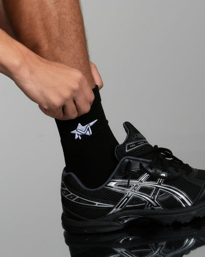 Person putting on a black sock with a logo on a gray background